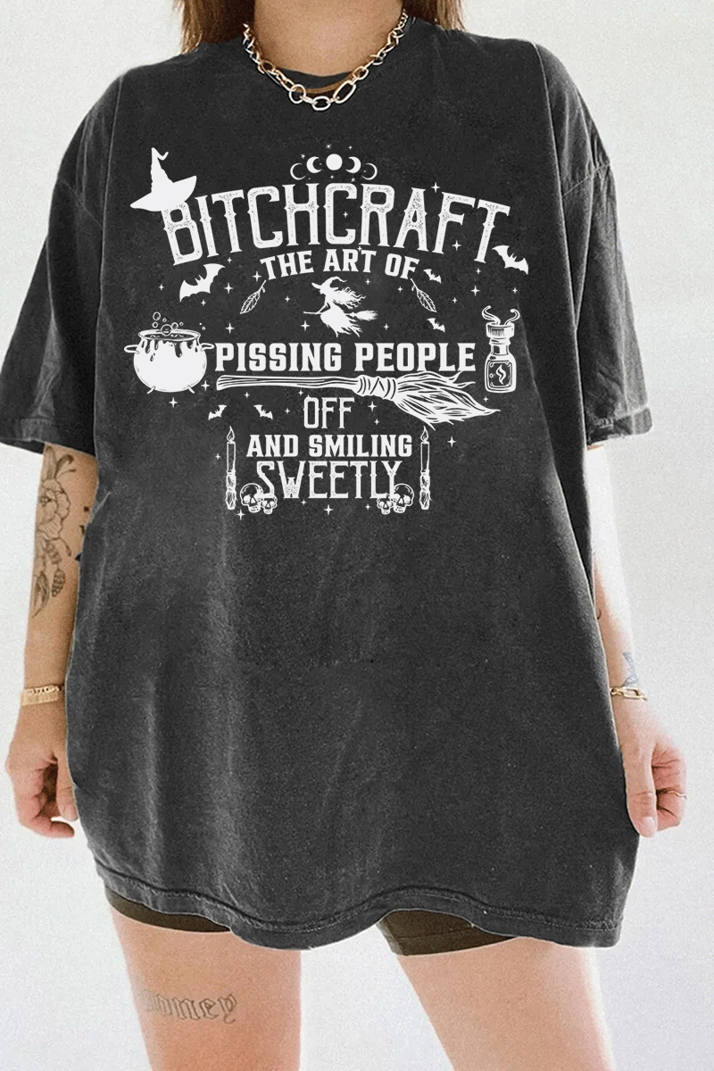 Witchcraft-themed Bitchcraft graphic with symbols including a flying witch, broomstick, potion bottle, and the text 'The Art of Pissing People Off and Smiling Sweetly,' printed on a dark gray T-shirt from Ragglo.