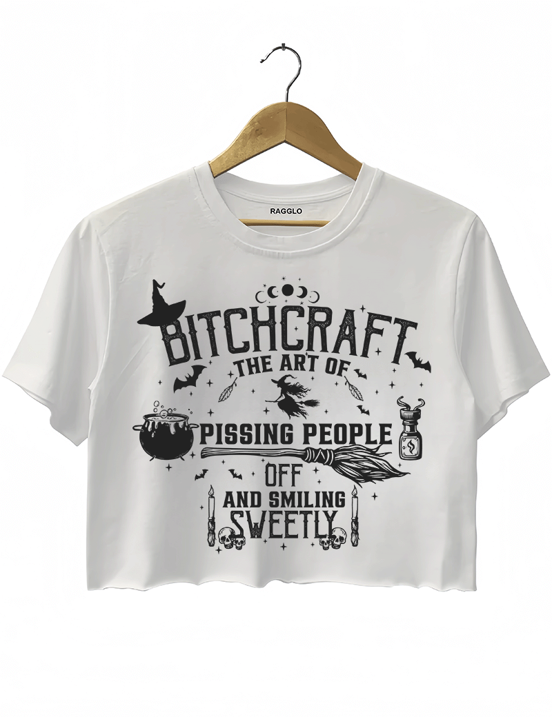 Bitchcraft design with the text 'The Art of Pissing People Off and Smiling Sweetly,' surrounded by witchcraft symbols like a witch hat, cauldron, broom, and skulls, printed on a white crop top available at Ragglo.