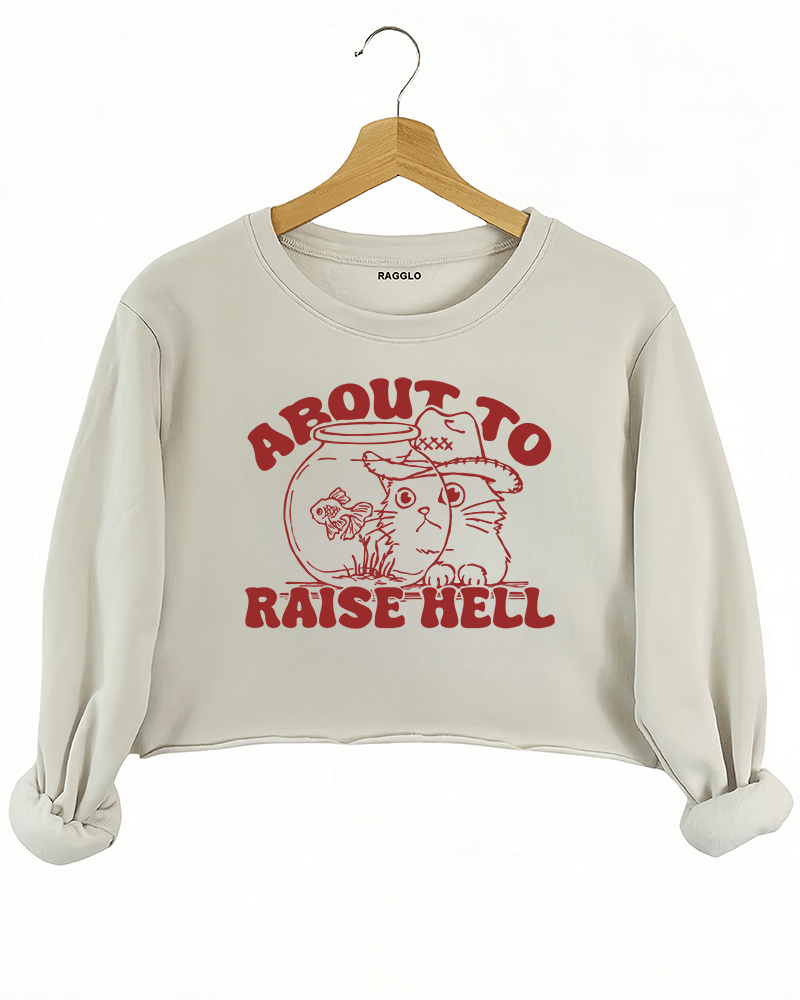 Ragglo beige women's crop sweatshirt with 'About to Raise Hell' text and cat in cowboy hat graphic.