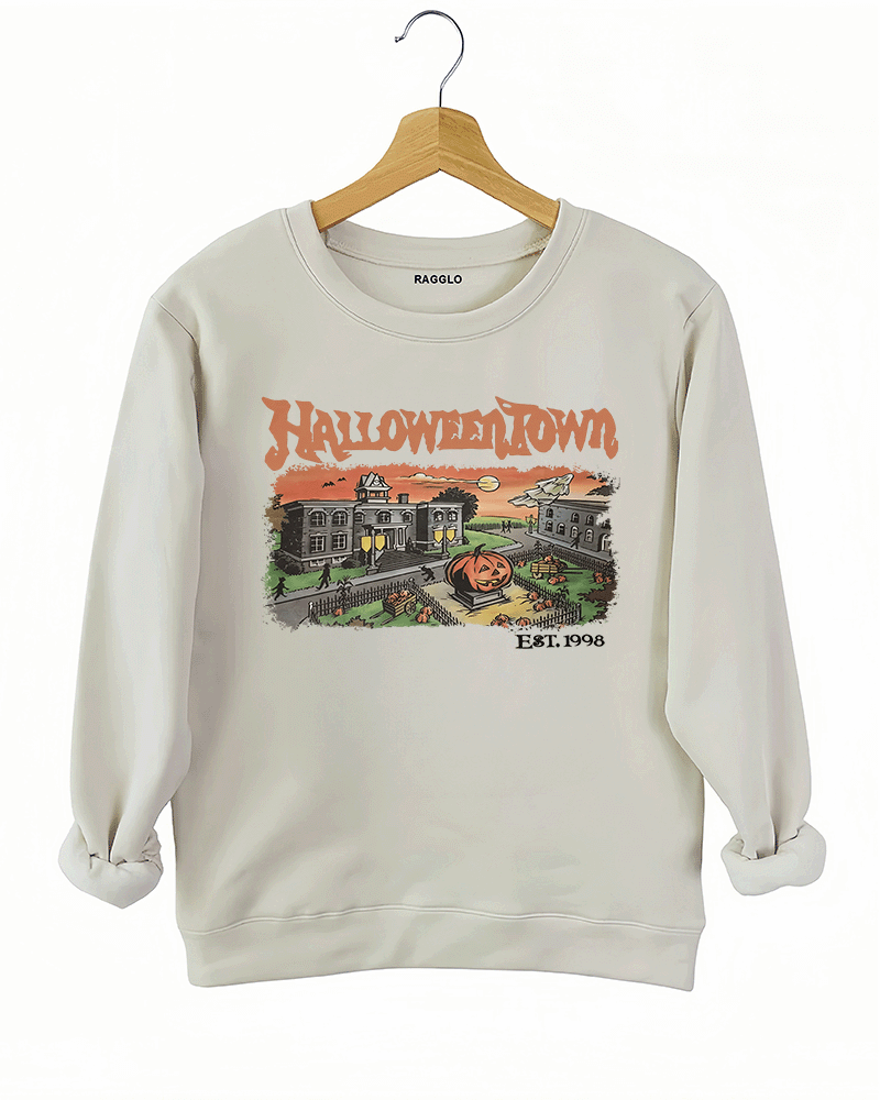 Ragglo beige women's sweatshirt featuring a spooky town with a jack-o'-lantern, graveyard, and old houses under a sunset sky with bats, and the text 'Halloween Town Est. 1998' in a retro Halloween graphic design.