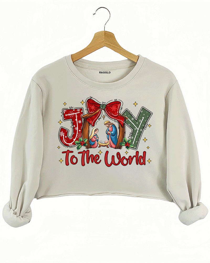 Ragglo beige crop sweatshirt featuring 'JOY TO THE WORLD' text with a nativity scene, a red bow, and holly leaves, perfect for religious Christmas streetwear and festive celebrations.