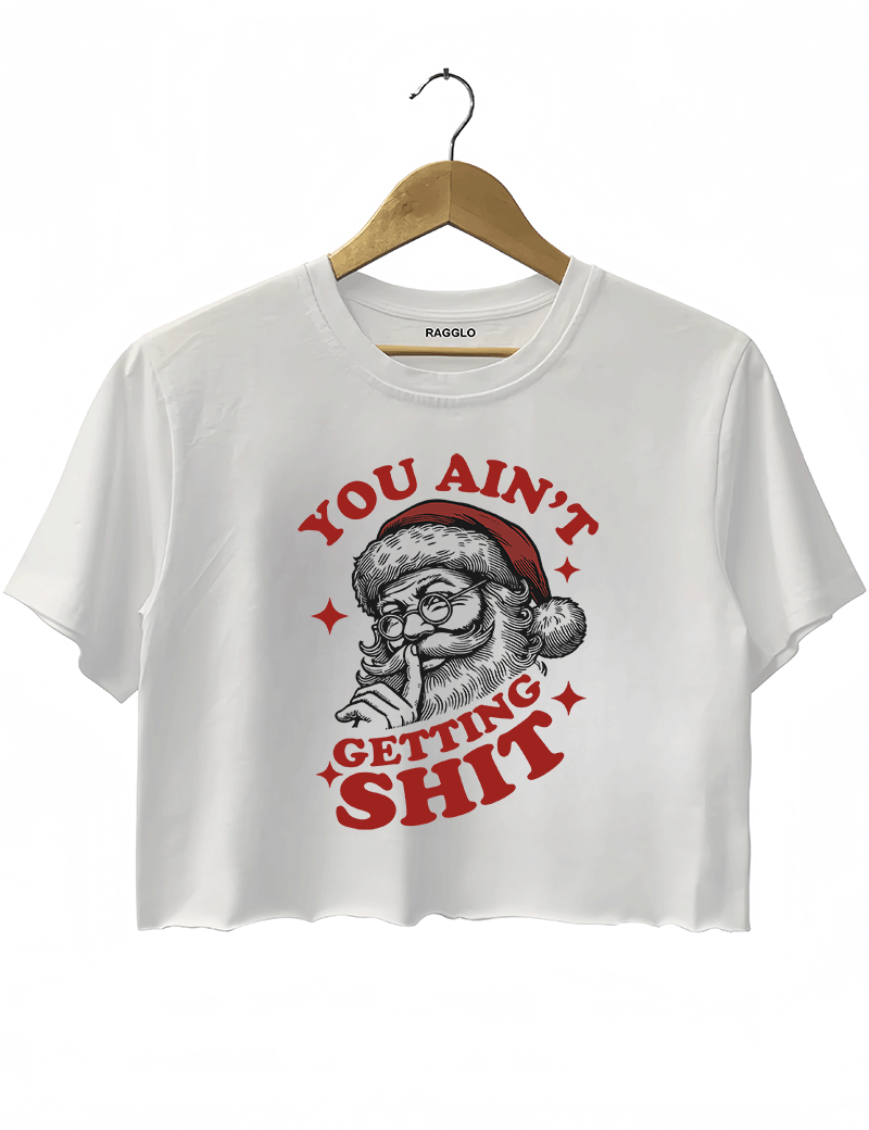 White Ragglo women's crop top featuring a bold Santa Claus graphic with the text "YOU AIN'T GETTING SHIT" in a striking red and black color scheme, hanging on a wooden hanger.