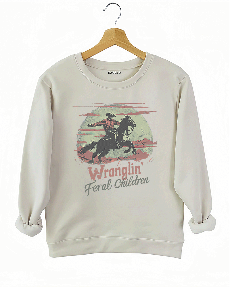 Ragglo beige women's sweatshirt featuring a cowboy riding a horse under a moonlit mountain background with the humorous text 'Wranglin' Feral Children' in a playful western graphic design.