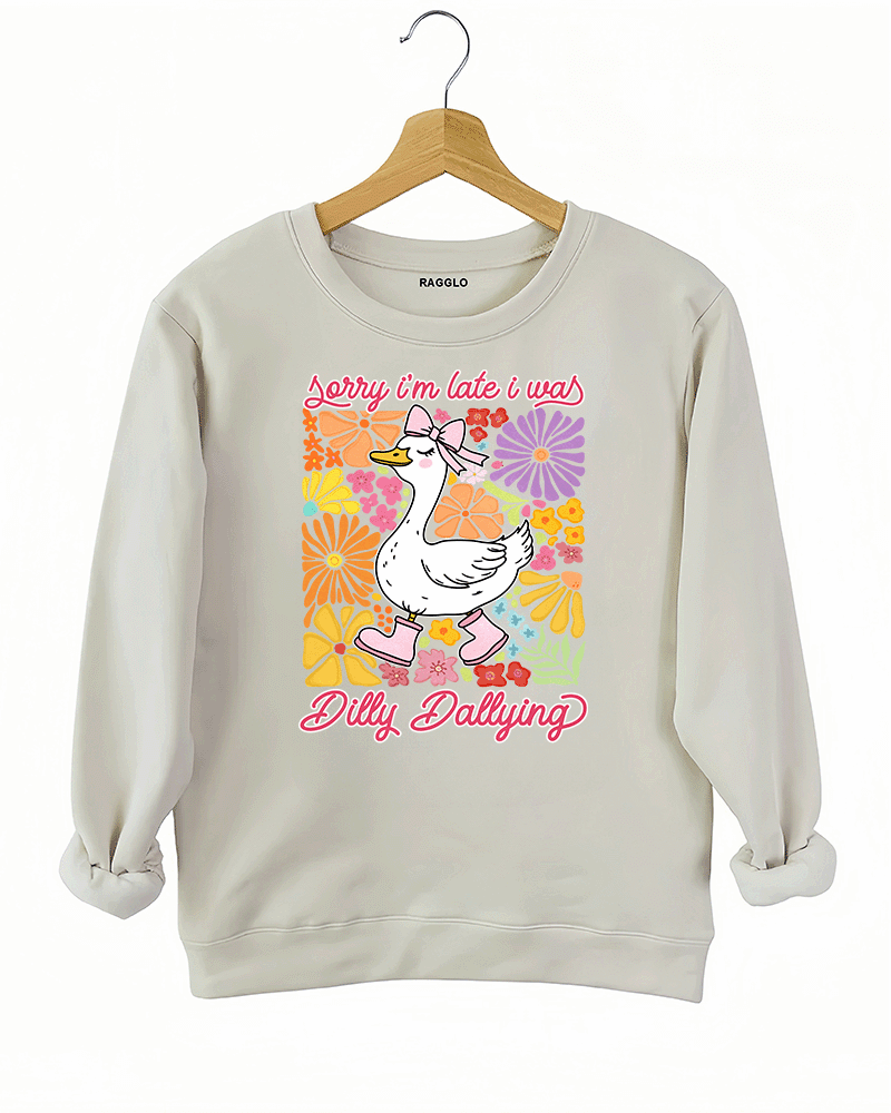 Ragglo beige sweatshirt featuring a cute duck in pink rain boots and a bow, surrounded by vibrant flowers, with 'Sorry I'm Late I Was Dilly Dallying' text, perfect for playful floral-inspired casual wear.