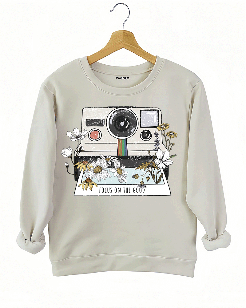 Ragglo beige sweatshirt featuring a vintage Polaroid camera surrounded by flowers, with 'FOCUS ON THE GOOD' text, perfect for retro-inspired streetwear with a positive vibe.