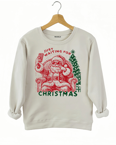 Ragglo beige sweatshirt featuring a Santa selfie graphic with sunglasses, a Christmas tree, and 'JUST WAITING FOR CHRISTMAS' text, perfect for festive holiday streetwear and fun celebrations.