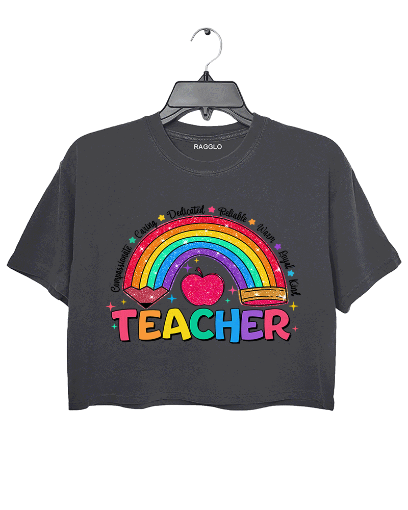 Ragglo dark gray crop top featuring a glittery rainbow with a heart and pencil, surrounded by words like 'Compassionate' and 'Caring', with 'TEACHER' text, perfect for educators and teacher appreciation streetwear.