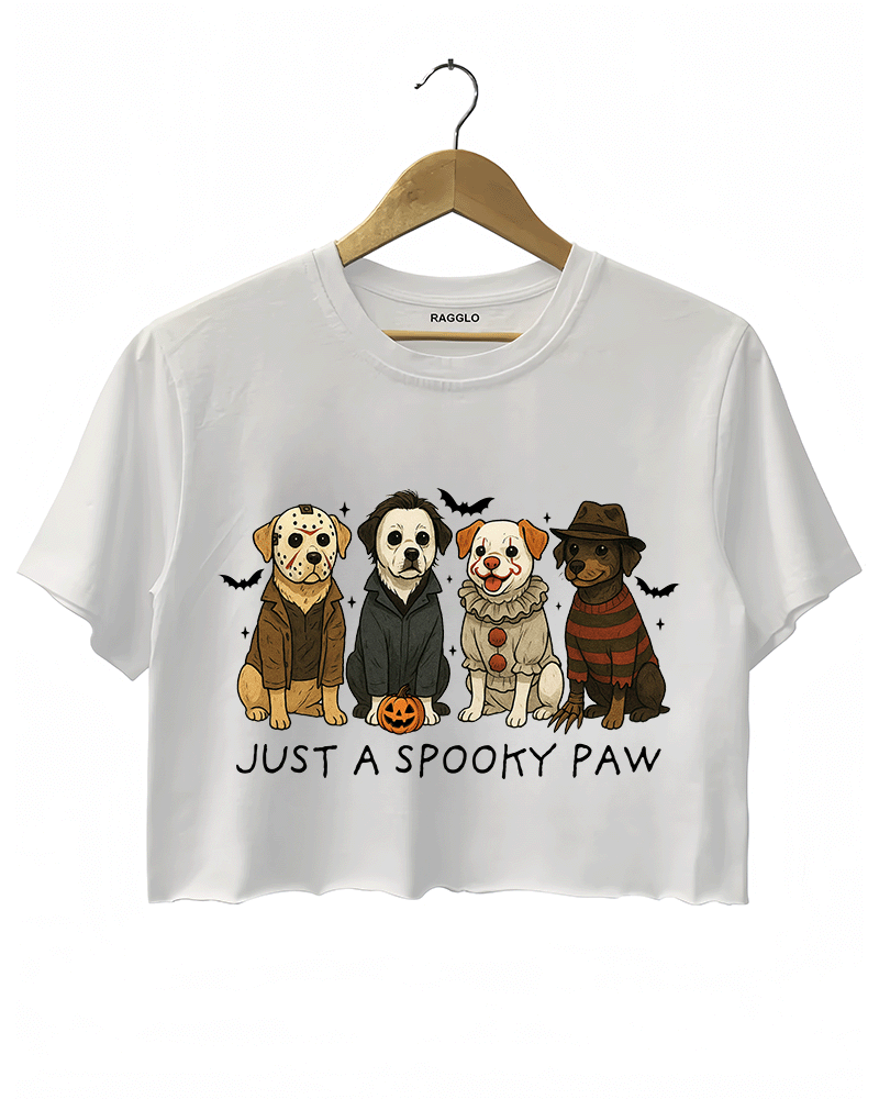 White cropped T-shirt by RAGGLO showcasing four adorable cartoon dogs in Halloween horror costumes, styled after classic characters like Freddy Krueger, Michael Myers, Pennywise, and Billy the Puppet. Accented with bats and a pumpkin, and the phrase "JUST A SPOOKY PAW" beneath the artwork. A fun and festive piece for Halloween lovers.
