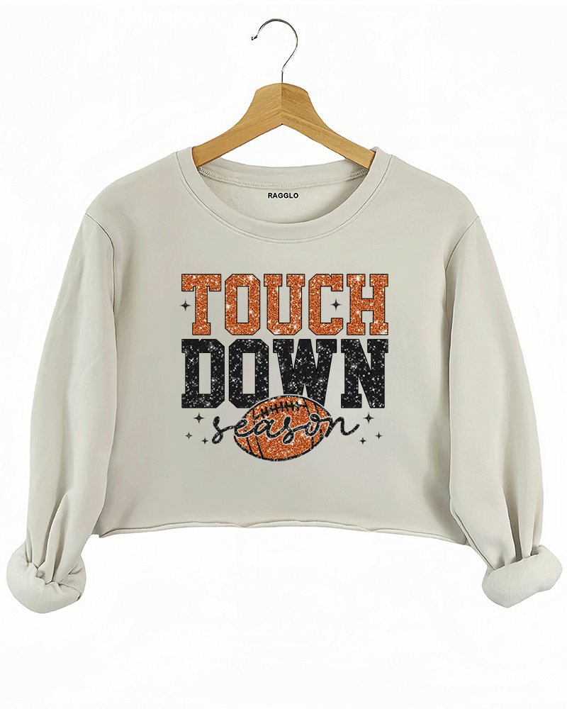 Ragglo beige crop sweatshirt featuring 'TOUCH DOWN' text with a football graphic and 'season' script, accented by stars, perfect for football fans and game day streetwear.