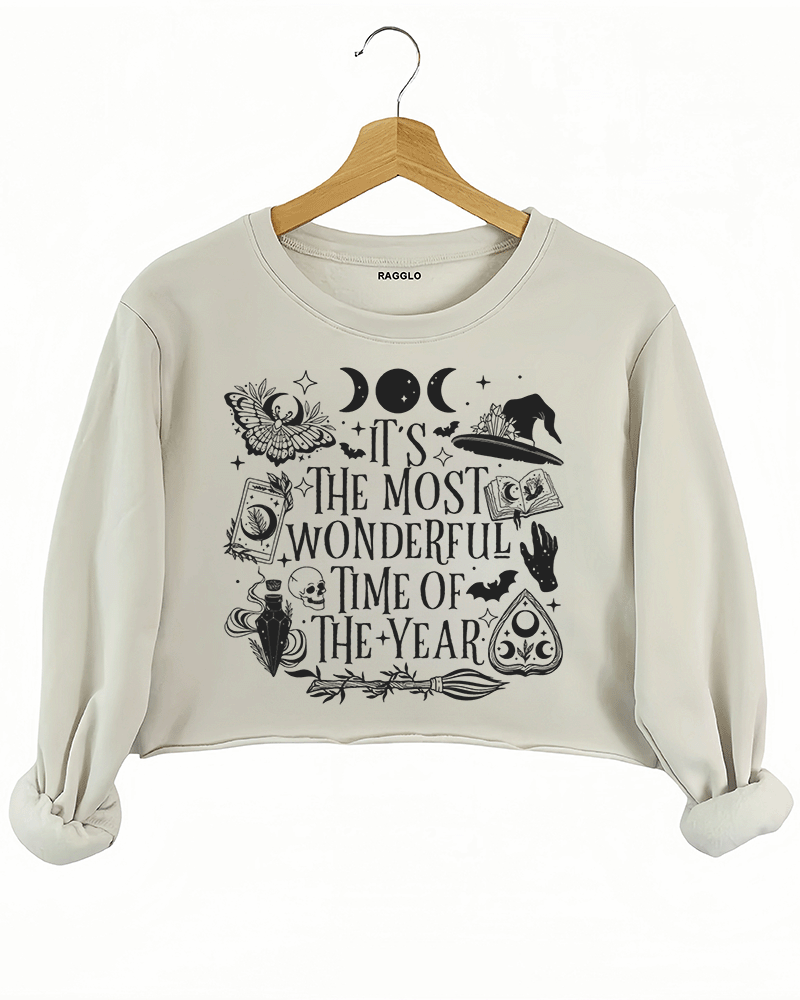 Ragglo beige crop sweatshirt featuring witchy elements like moons, bats, a witch hat, spellbook, and potion bottle, with 'IT’S THE MOST WONDERFUL TIME OF THE YEAR' text, perfect for magical Halloween streetwear.