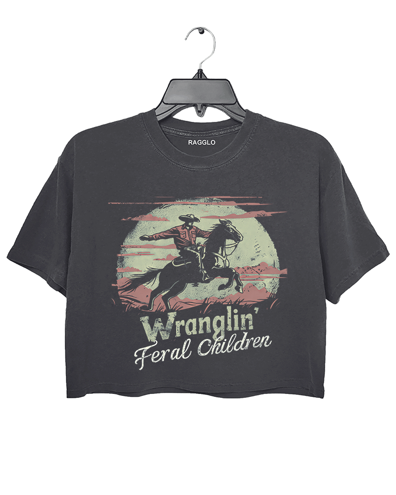Ragglo dark gray women's crop top featuring a cowboy riding a horse under a moonlit mountain background with the humorous text 'Wranglin' Feral Children' in a playful western graphic design.