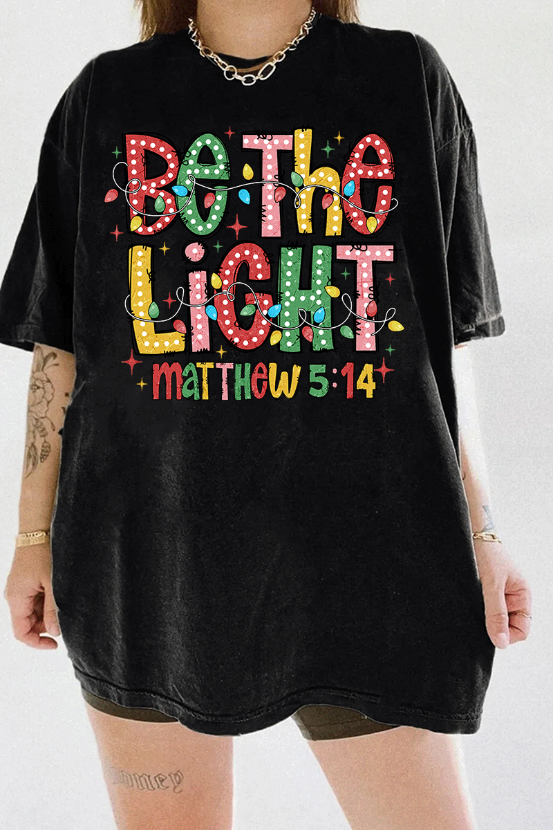 Be the Light - Matthew 5:14 design with vibrant colors and Christmas lights on a black T-shirt, available on Ragglo.