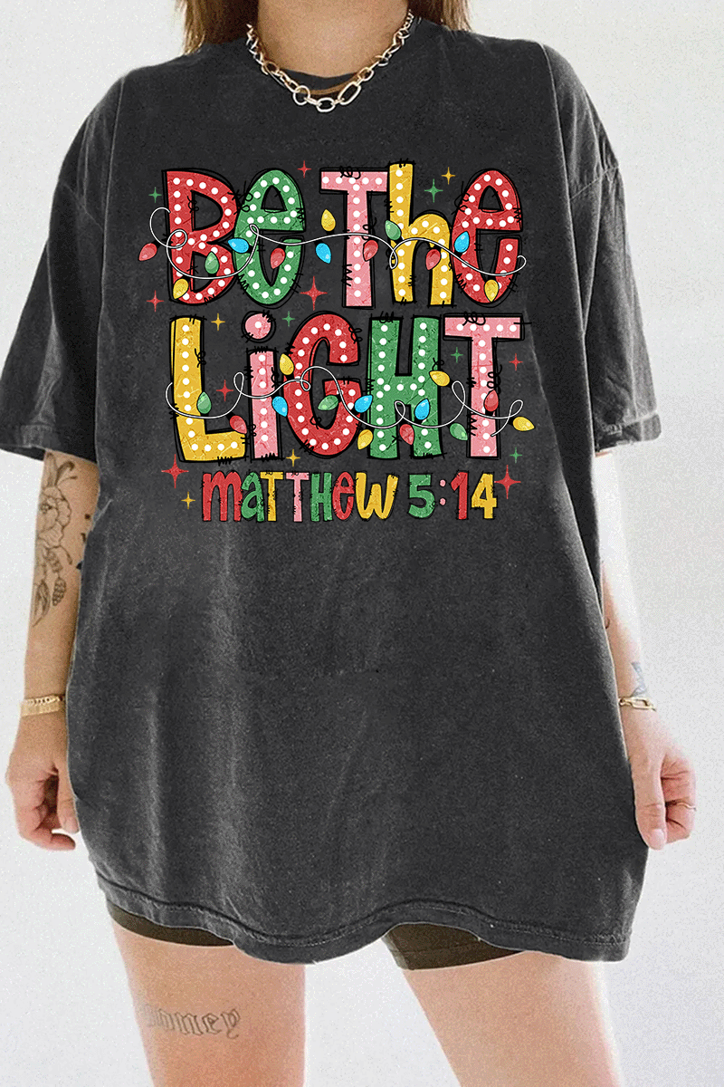 Be the Light - Matthew 5:14 design with vibrant colors and Christmas lights on a dark gray T-shirt, available on Ragglo.