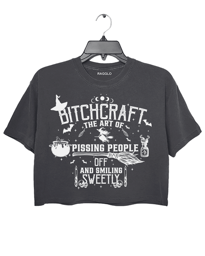 Bitchcraft graphic featuring the phrase 'The Art of Pissing People Off and Smiling Sweetly,' with witchcraft elements like a cauldron, broom, flying witch, and magic potion, printed on a dark gray crop top - available on Ragglo.