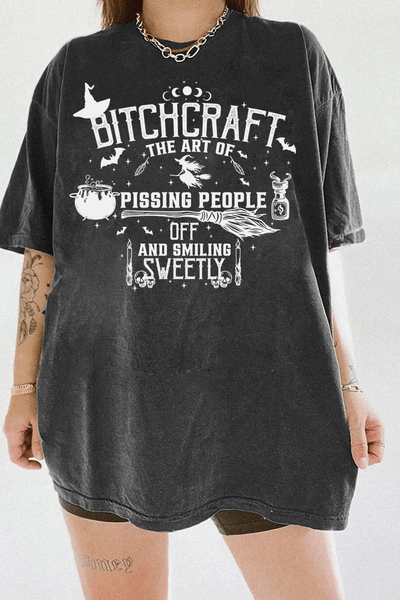 Witchcraft-themed Bitchcraft graphic with symbols including a flying witch, broomstick, potion bottle, and the text 'The Art of Pissing People Off and Smiling Sweetly,' printed on a dark gray T-shirt from Ragglo.