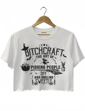 Bitchcraft design with the text 'The Art of Pissing People Off and Smiling Sweetly,' surrounded by witchcraft symbols like a witch hat, cauldron, broom, and skulls, printed on a white crop top available at Ragglo.