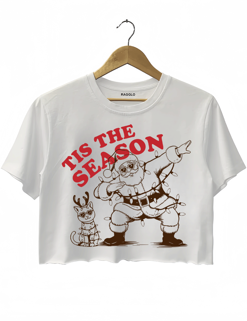 Fun Tis The Season design showing Santa doing a dab, wearing heart-shaped sunglasses and wrapped in Christmas lights, with a festive cat, printed on a white crop top available at Ragglo.