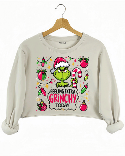 Beige crop sweatshirt featuring the iconic Grinch with a Santa hat and candy cane, set against a backdrop of holiday ornaments, available on Ragglo.