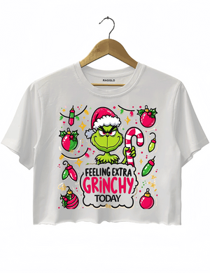 White crop top showcasing the mischievous Grinch wearing a Santa hat and holding a candy cane, with a playful Christmas ornament background, available on Ragglo.