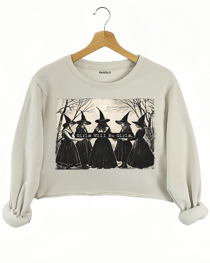 Beige crop sweatshirt with a graphic of five witches in traditional dresses and pointed hats, standing in a dark forest, paired with the phrase 'Girls Will Be Girls,' available on Ragglo.