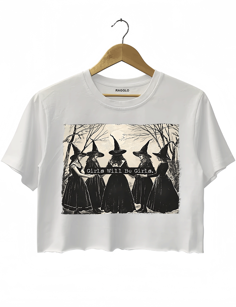 White crop top showcasing five witches in gothic gowns and hats, standing with their backs turned in a mysterious forest, along with the phrase 'Girls Will Be Girls,' available on Ragglo.