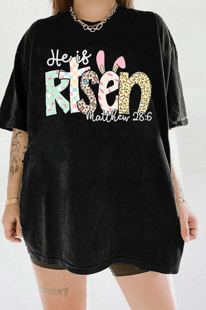 Black women's T-shirt from Ragglo with "He is Risen" and "Matthew 28:6" text, featuring Easter-themed bunny and egg patterns in pastel colors.

