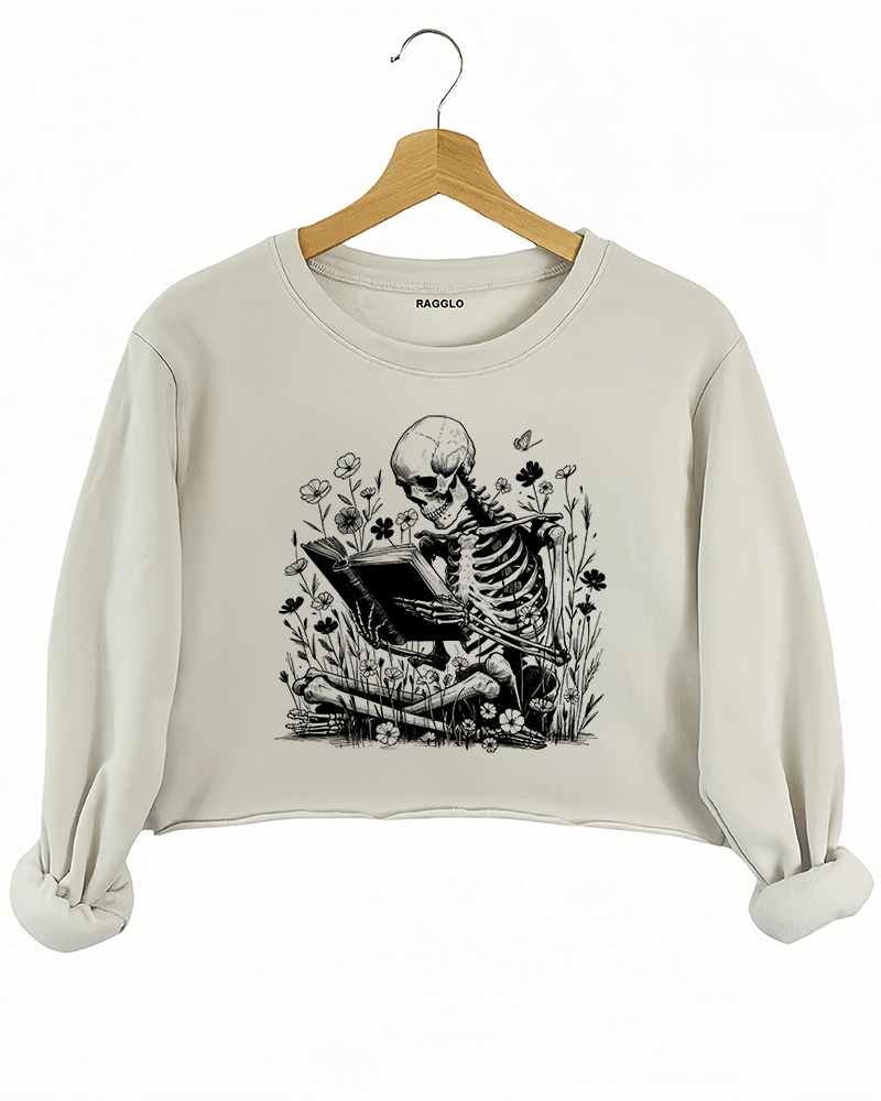 Ragglo beige crop sweatshirt with skeleton reading book graphic surrounded by flowers and butterflies

