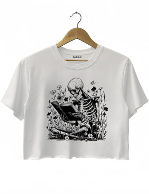 Ragglo white crop top with skeleton reading book graphic surrounded by flowers and butterflies.

