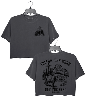 Ragglo dark gray women's crop top featuring a minimalist cross and trees design on the front, and a mountain landscape with cattle, a cross, and trees on the back with the text 'Follow The Word Not The Herd' and 'Isaiah 8:11-13' in a faith-inspired graphic design.