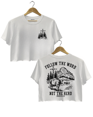 Ragglo white women's cropped T-Shirt featuring a minimalist cross and trees design on the front, and a mountain landscape with cattle, a cross, and trees on the back with the text 'Follow The Word Not The Herd' and 'Isaiah 8:11-13' in a faith-inspired graphic design.