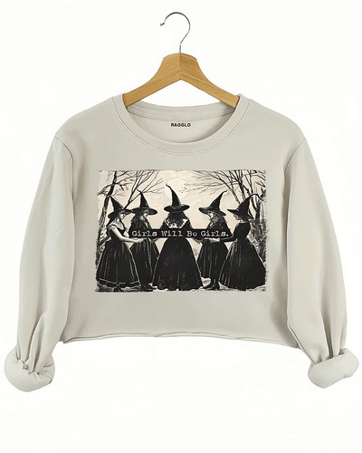 Ragglo beige women's crop sweatshirt featuring five witches in black hats holding a sign with the text 'Girls Will Be Girls' in a spooky forest background.