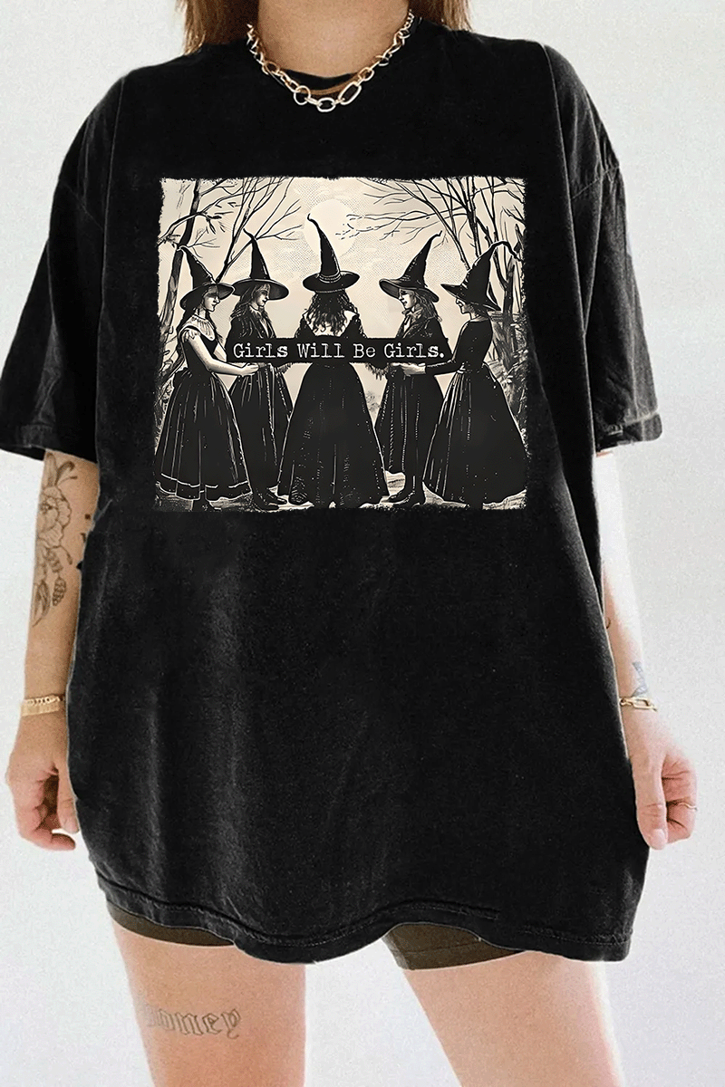 Ragglo black women's T-shirt featuring five witches in black hats holding a sign with the text 'Girls Will Be Girls' in a spooky forest background.