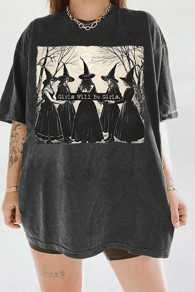 Ragglo dark gray women's T-shirt featuring five witches in black hats holding a sign with the text 'Girls Will Be Girls' in a spooky forest background.