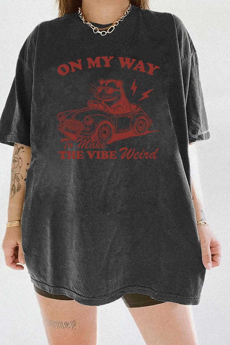 Ragglo dark gray women's t-shirt with 'On My Way to Make the Vibe Weird' text and raccoon driving car graphic.

