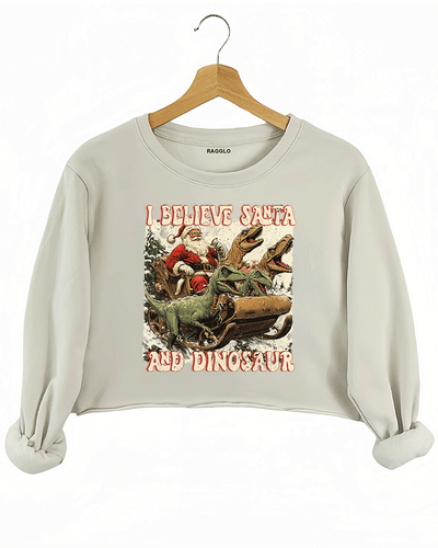 Ragglo beige women's crop sweatshirt with 'I Believe Santa and Dinosaur' text and Santa sleigh pulled by dinosaurs graphic.

