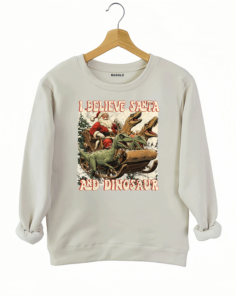 Ragglo beige women's sweatshirt with 'I Believe Santa and Dinosaur' text and Santa sleigh pulled by dinosaurs graphic.

