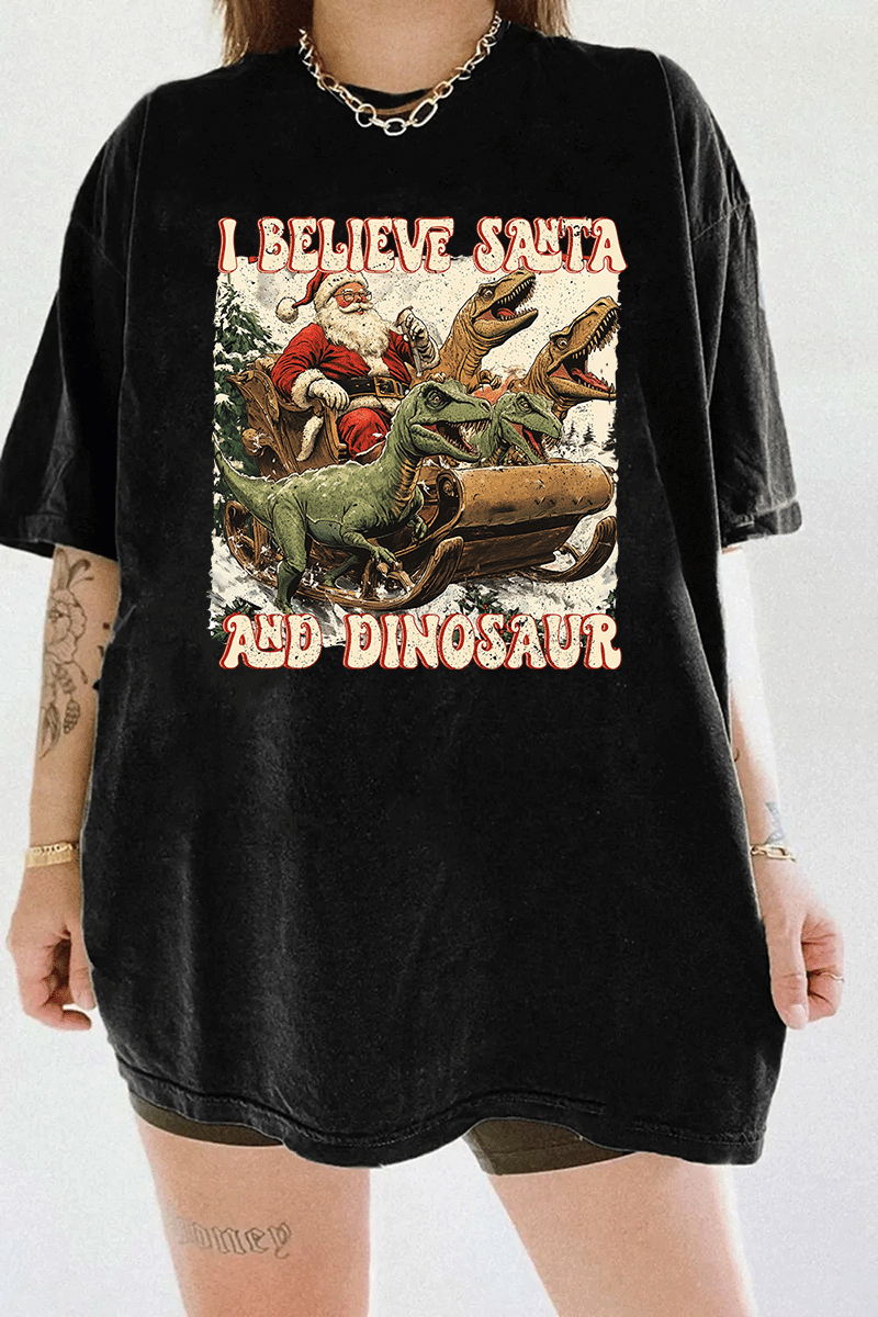 Ragglo black women's tee with 'I Believe Santa and Dinosaur' text and Santa sleigh pulled by dinosaurs graphic.

