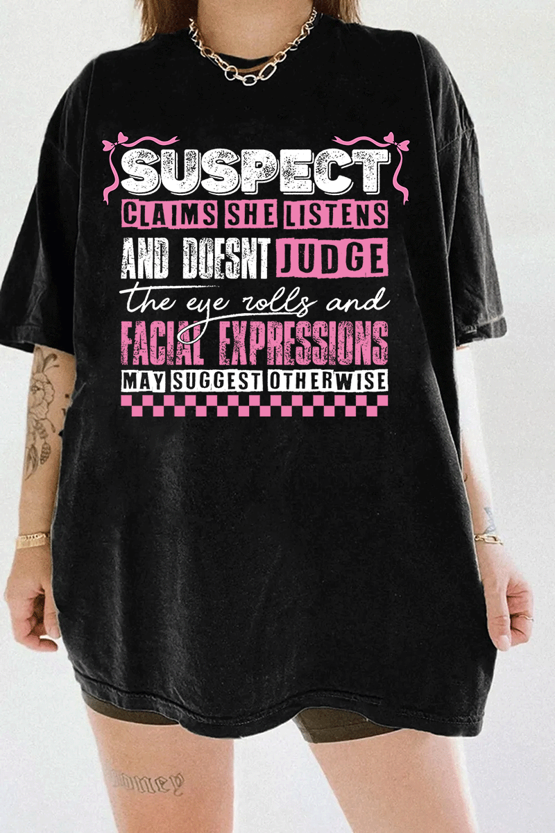 Black Ragglo women's t-shirt with pink 'Suspect' design, featuring playful text: 'Claims she listens and doesn't judge, the eye rolls and facial expressions may suggest otherwise.

