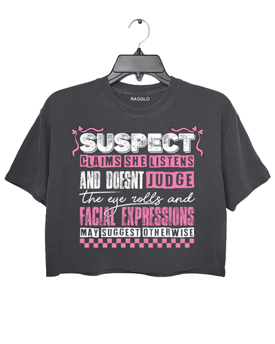 Dark gray Ragglo women's crop t-shirt with pink 'Suspect' design, featuring playful text: 'Claims she listens and doesn't judge, the eye rolls and facial expressions may suggest otherwise.

