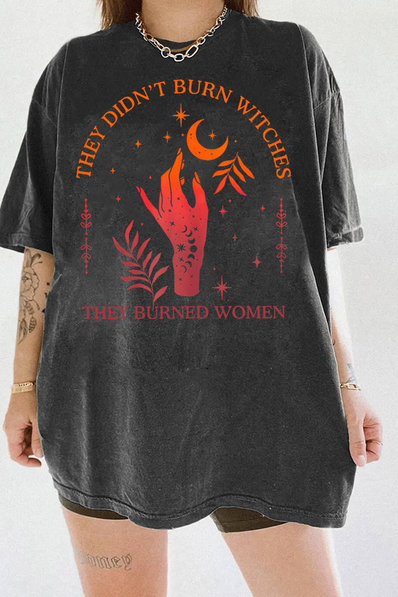 Ragglo dark gray women's T-shirt with 'They Didn’t Burn Witches, They Burned Women' text and flaming hand with mystical symbols graphic.

