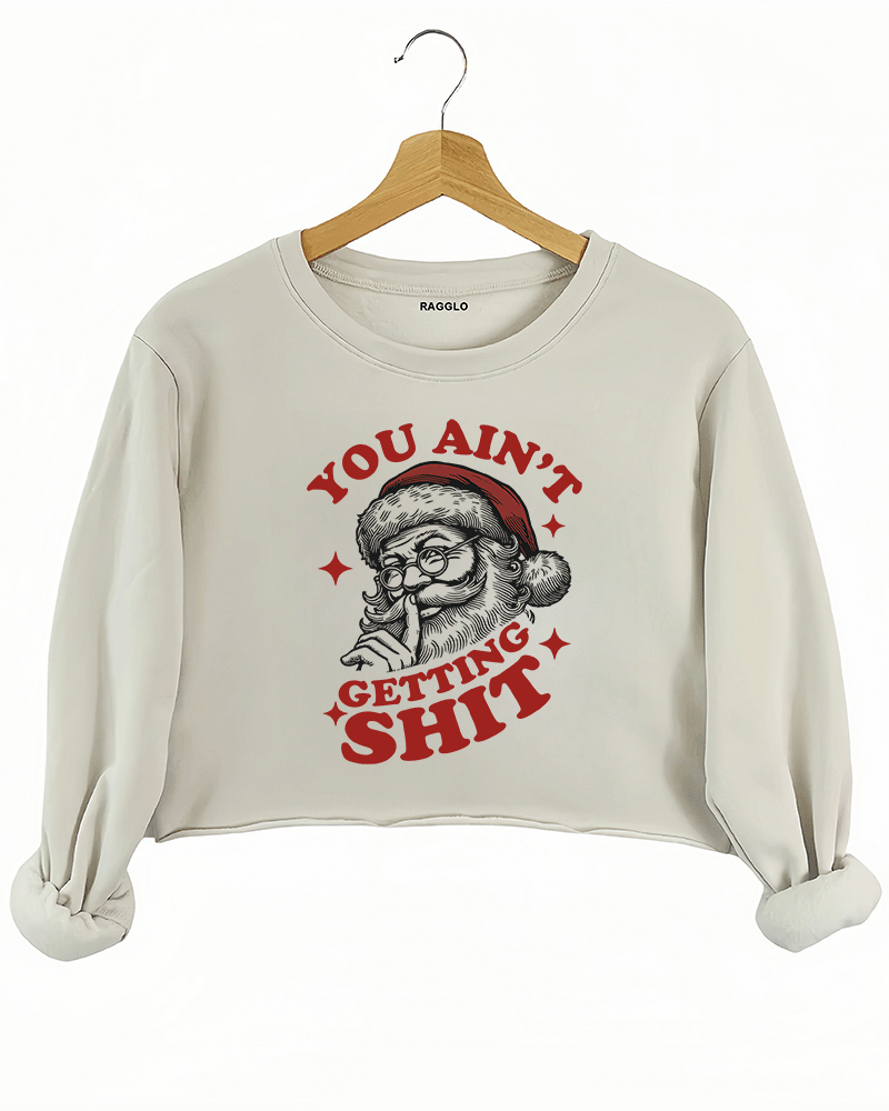 Cozy beige Ragglo women's crop sweatshirt featuring a Santa Claus graphic with the text "YOU AIN'T GETTING SHIT" in bold red and black, hanging on a wooden hanger.

