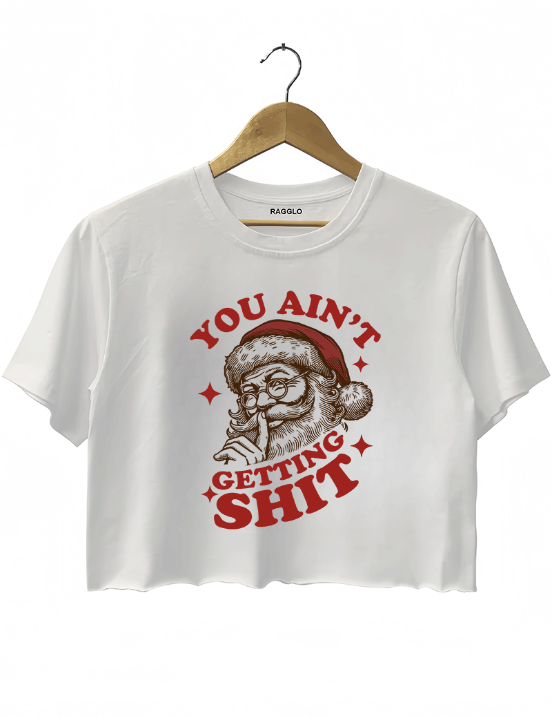 White Ragglo women's crop top featuring a bold Santa Claus graphic with the text "YOU AIN'T GETTING SHIT" in a striking red and brown color scheme, hanging on a wooden hanger.

