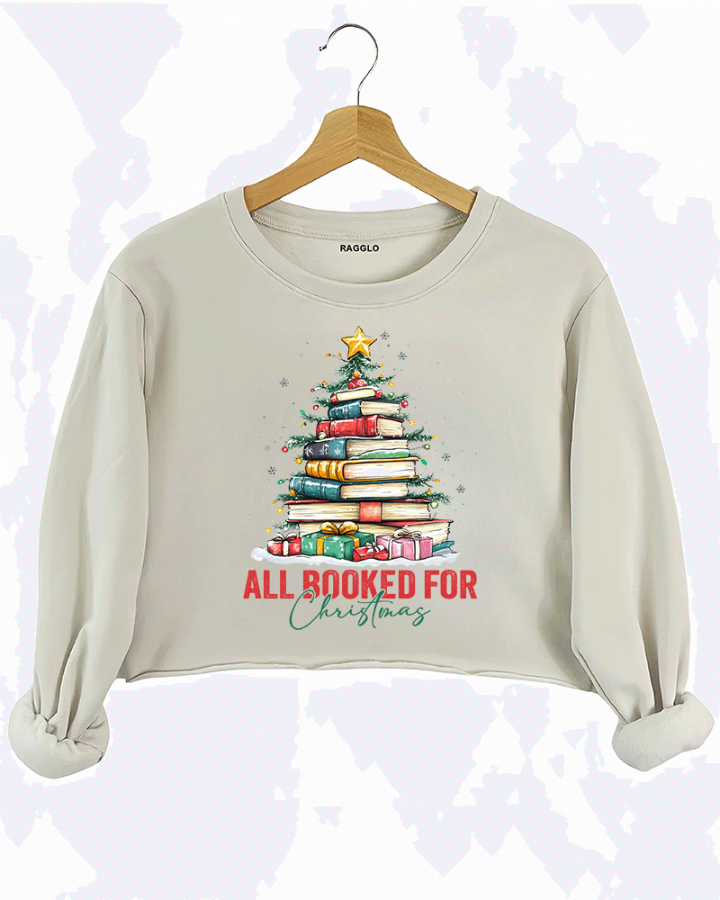 Ragglo beige crop sweatshirt featuring a Christmas tree made of stacked books, decorated with lights, stars, and gifts, with 'ALL BOOKED FOR CHRISTMAS' text, perfect for festive streetwear for book lovers.

