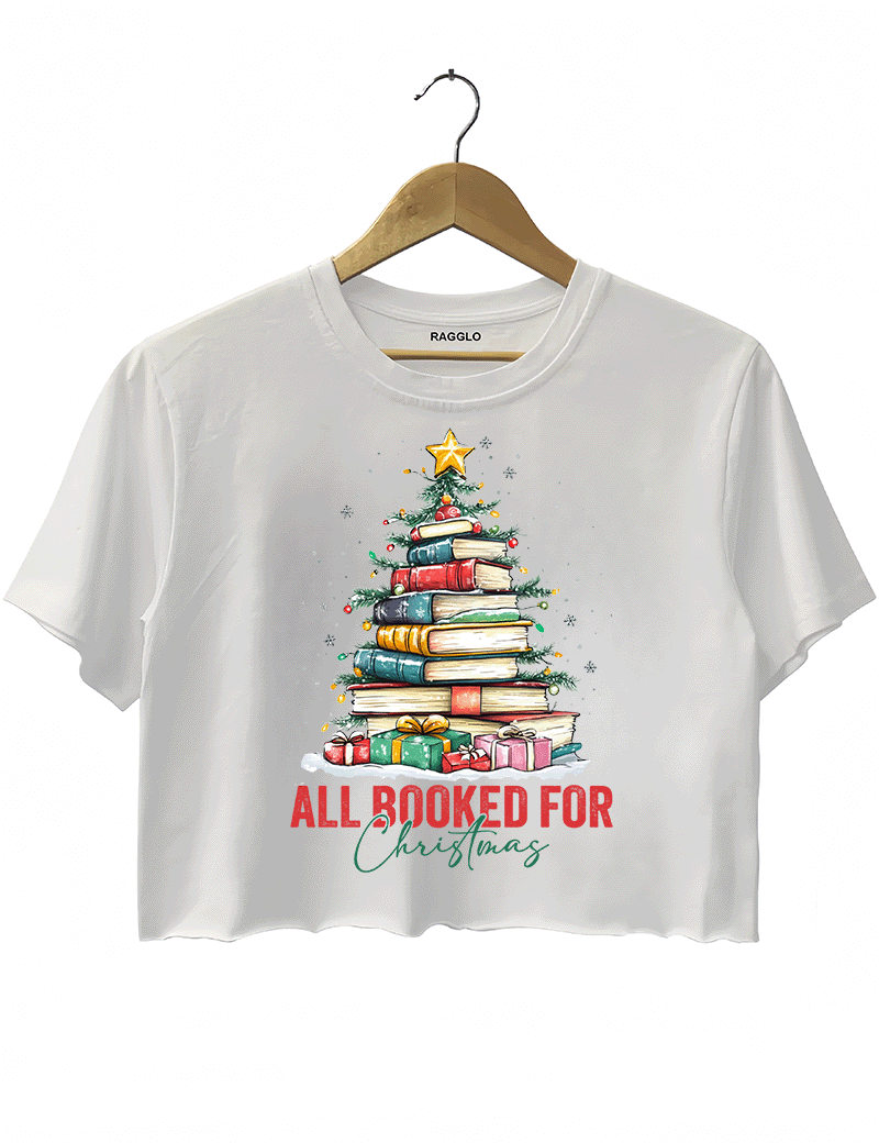 Ragglo white crop top featuring a Christmas tree made of stacked books, decorated with lights, stars, and gifts, with 'ALL BOOKED FOR CHRISTMAS' text, perfect for festive streetwear for book lovers.

