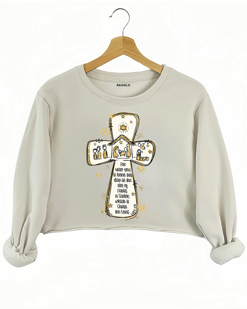 Ragglo beige crop sweatshirt featuring a cross with a nativity scene, stars, and snowflakes, with 'Unto you is born this day in the city of David, a Savior which is Christ the Lord' text, perfect for religious Christmas streetwear.

