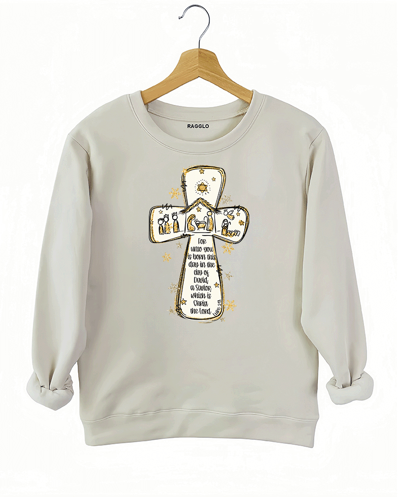 Ragglo beige sweatshirt featuring a cross with a nativity scene, stars, and snowflakes, with 'Unto you is born this day in the city of David, a Savior which is Christ the Lord' text, perfect for religious Christmas streetwear.

