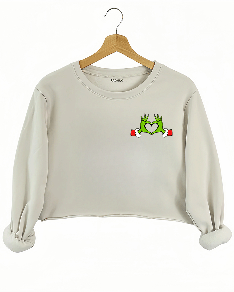 Ragglo beige women's crop sweatshirt front featuring Grinch hands making a heart shape with Santa cuffs in a playful Christmas design.