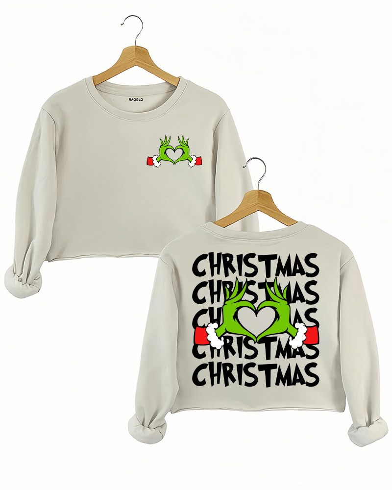 Ragglo beige women's crop sweatshirt featuring Grinch hands making a heart shape with Santa cuffs on the front, and larger Grinch hands with 'Christmas' text repeated around them on the back, in a funny holiday graphic design.