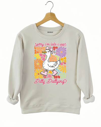 Ragglo beige sweatshirt featuring a cute duck in pink rain boots and a bow, surrounded by vibrant flowers, with 'Sorry I'm Late I Was Dilly Dallying' text, perfect for playful floral-inspired casual wear.

