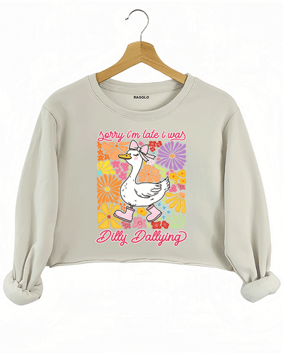 Ragglo beige crop sweatshirt featuring a cute duck in pink rain boots and a bow, surrounded by vibrant flowers, with 'Sorry I'm Late I Was Dilly Dallying' text, perfect for playful floral-inspired casual wear.

